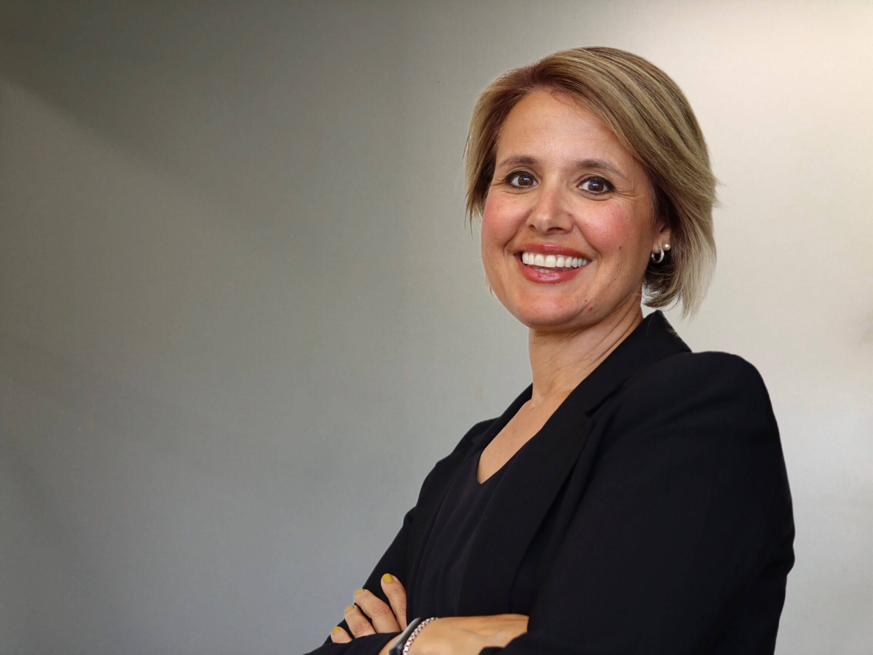 Smiling person in black blazer, arms crossed.